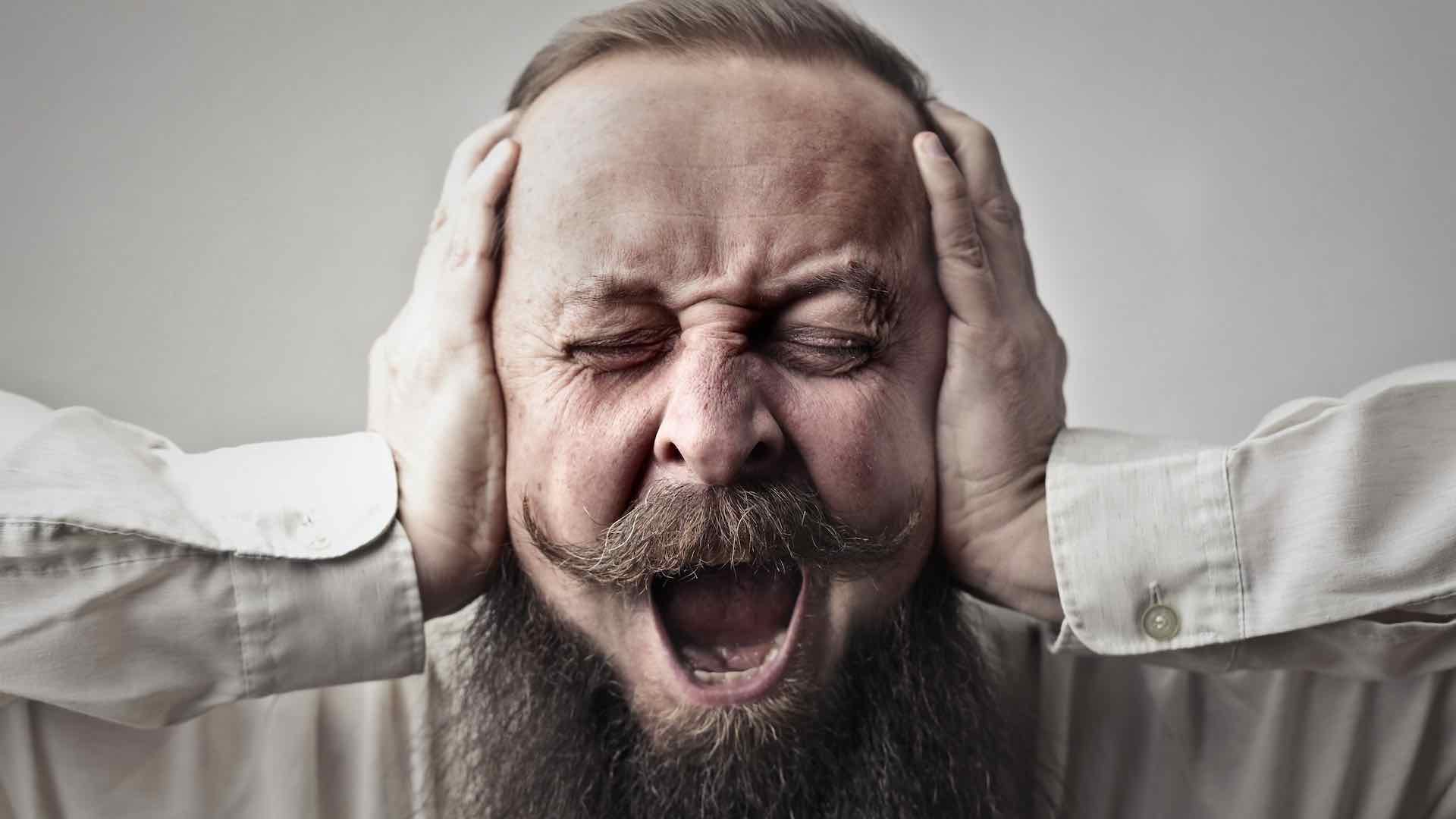 Un hombre tapándose la oreja y luciendo estresado.